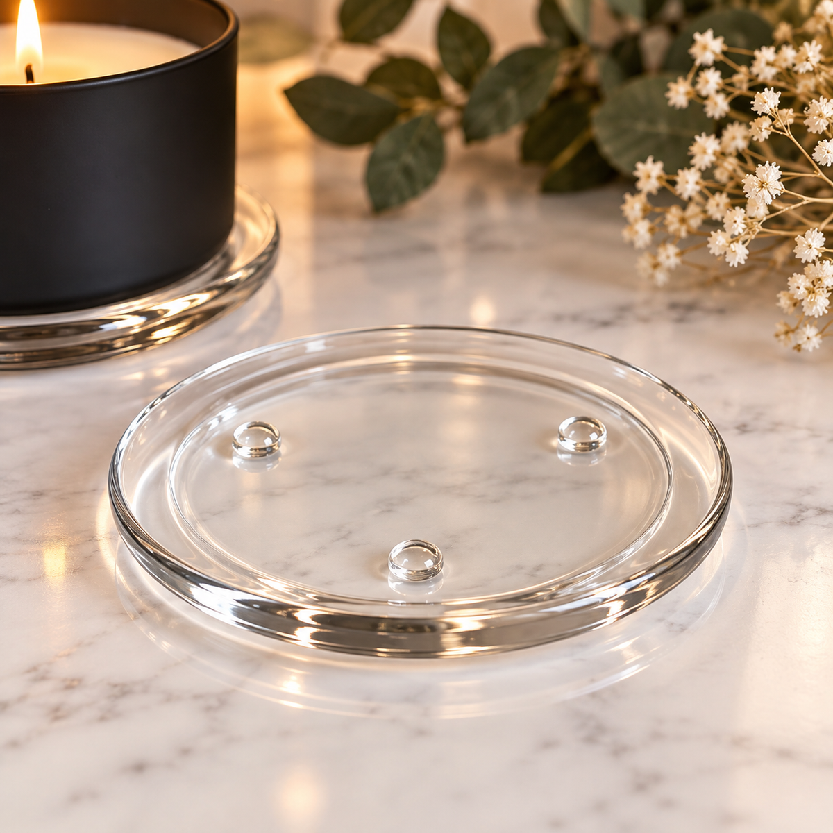 Clear glass candle plate with three raised feet on a marble surface (candle not included)